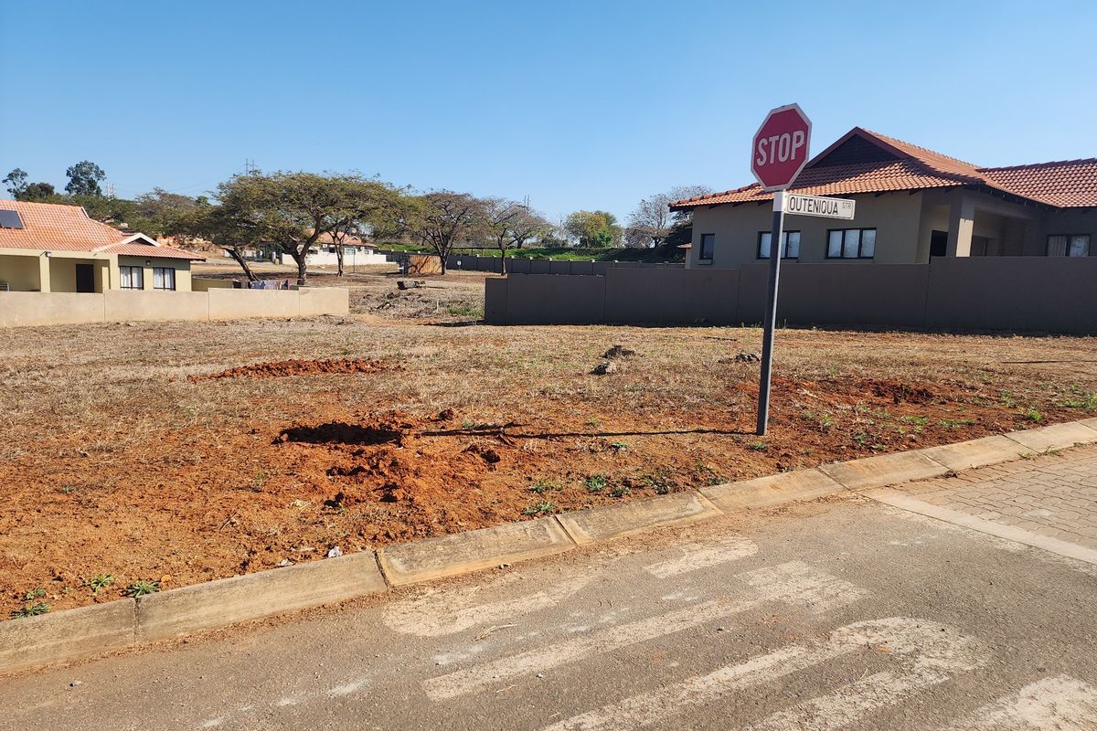 A vacant residential plot situated on a corner lot, featuring established boundary walls and street signage in a developed neighborhood.