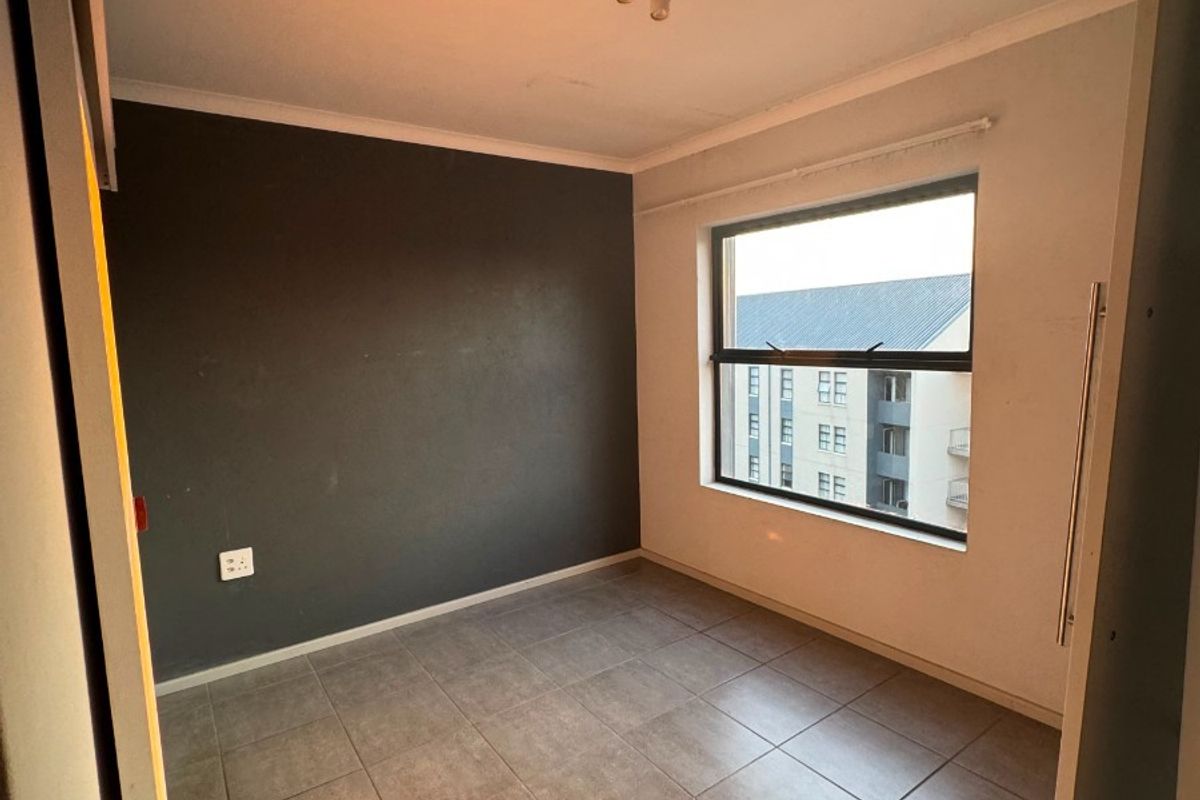 An empty bedroom featuring tiled flooring, a dark accent wall, and a built-in cupboard, offering a clean canvas for personalization.