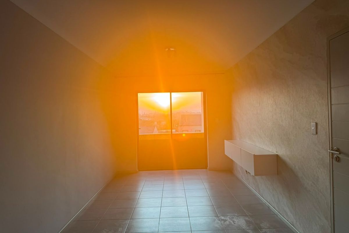 An empty living room featuring tiled flooring, a wall-mounted cabinet, and a sliding glass door with sunset views.