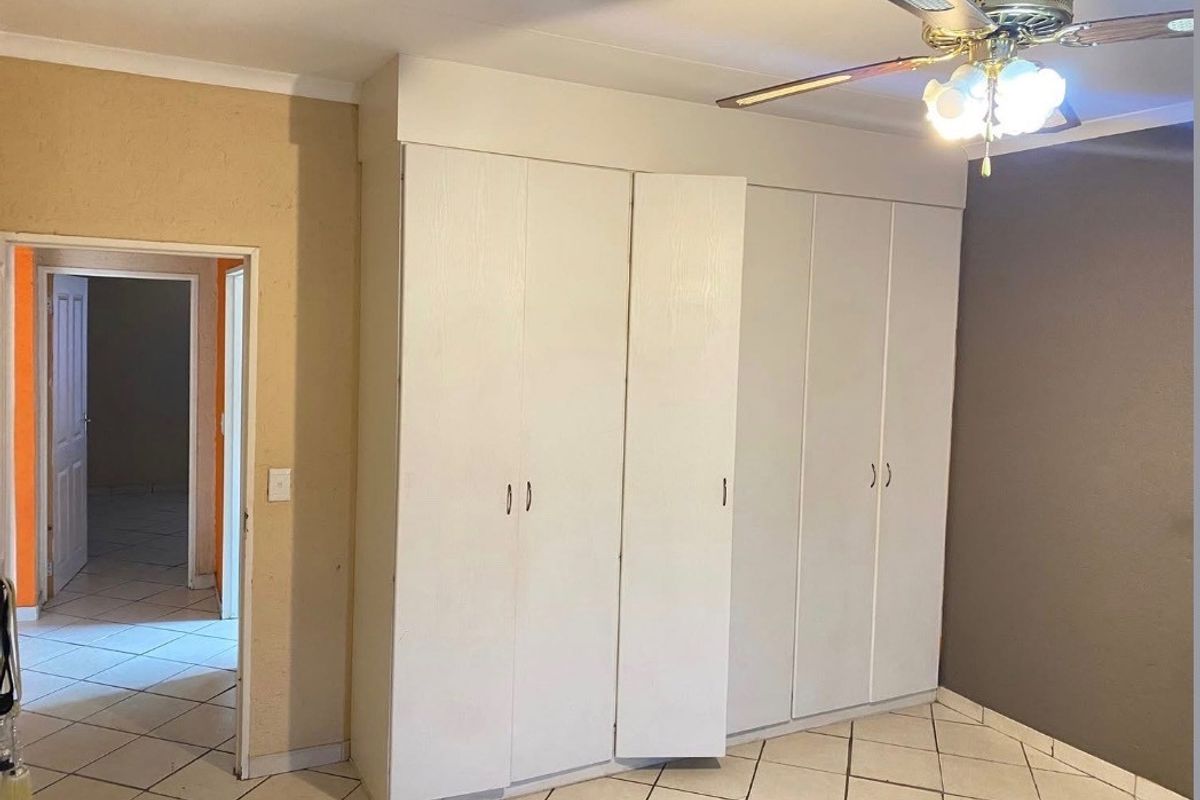 A vacant bedroom featuring built-in white cupboards, a ceiling fan, and tiled flooring, offering a neutral space ready for personalization.