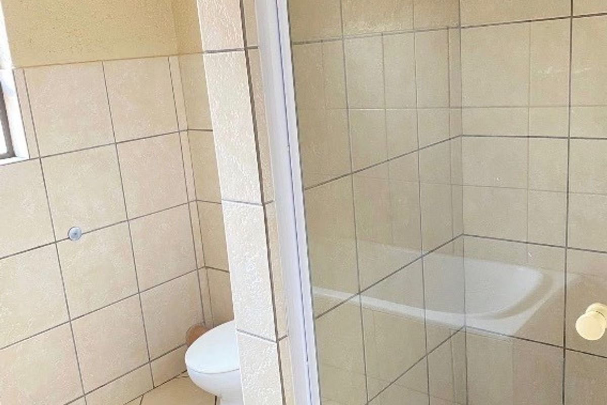 A functional bathroom featuring a glass-enclosed shower and a standard toilet with neutral ceramic wall and floor tiling.
