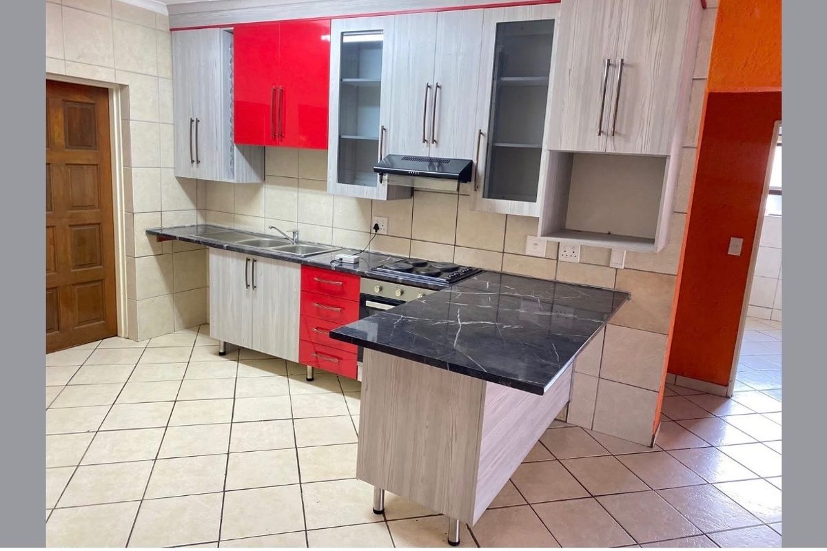 A functional kitchen featuring two-tone cabinetry, a black marble-effect countertop, built-in oven and hob, and tiled finishes throughout.