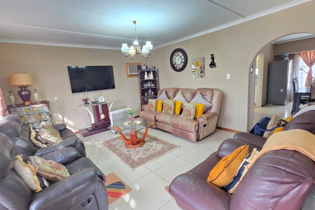 A spacious living room featuring tiled flooring, a decorative archway leading to the dining area, and a wall-mounted television.