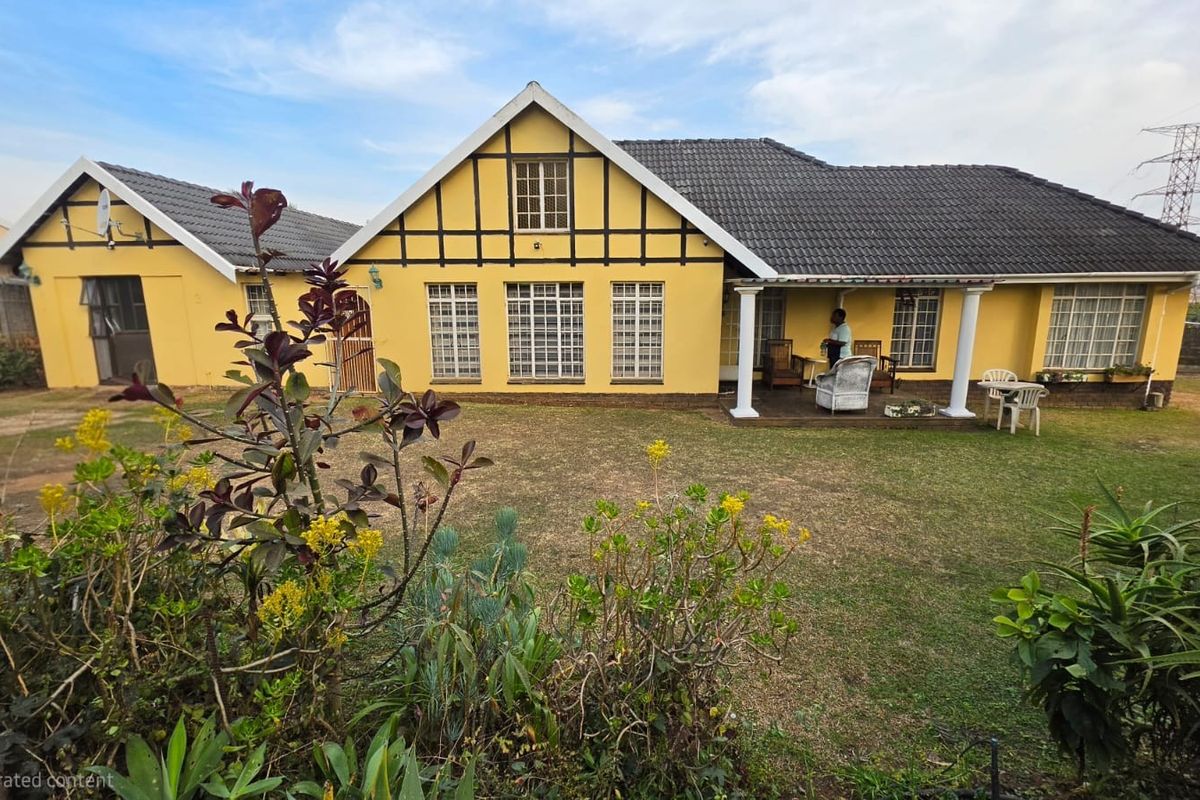 Rear view of a yellow house featuring a covered patio, tiled roof, and a spacious garden area.