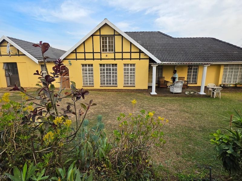Rear view of a yellow house featuring a covered patio, tiled roof, and a spacious garden area.