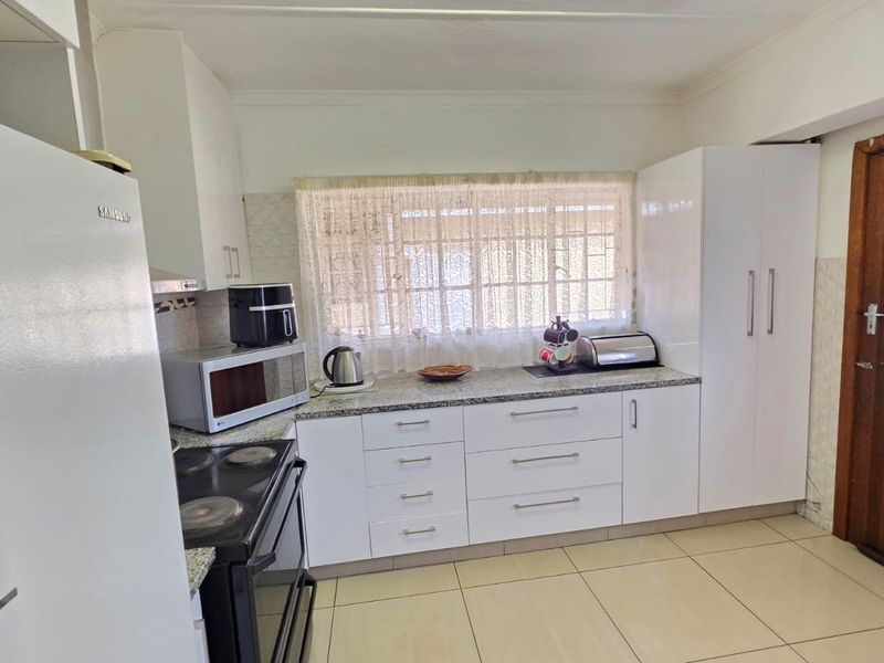 Functional kitchen featuring white cabinetry, granite countertops, tiled flooring, and an integrated stove with extractor fan.