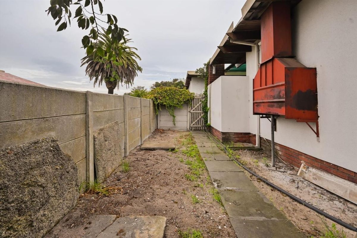 Rear exterior area featuring a precast concrete boundary wall, a paved walkway, and a built-in outdoor braai unit requiring maintenance.