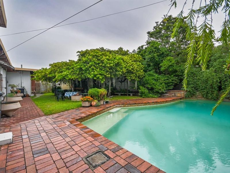Outdoor pool area featuring brick paving, a swimming pool, and a mature landscaped garden with established trees.