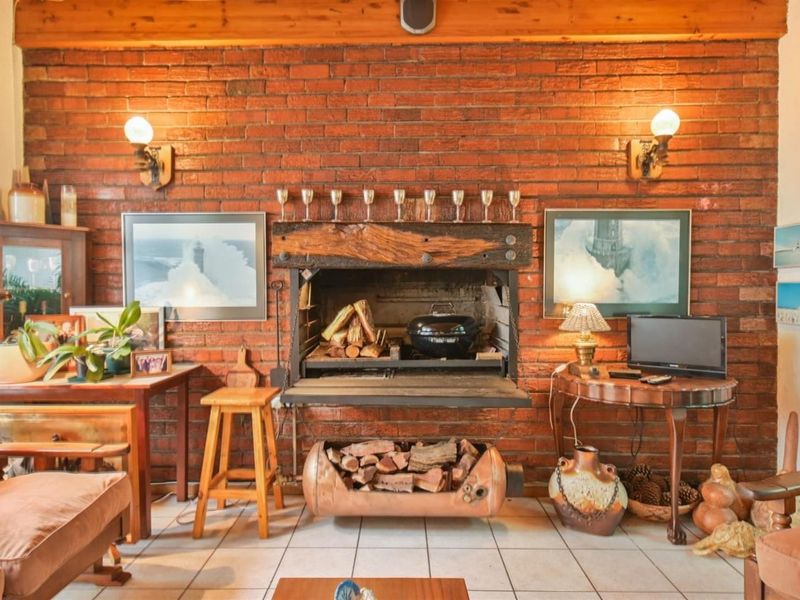 A living room featuring a prominent exposed brick wall with a built-in fireplace, timber mantelpiece, and ceramic floor tiles.