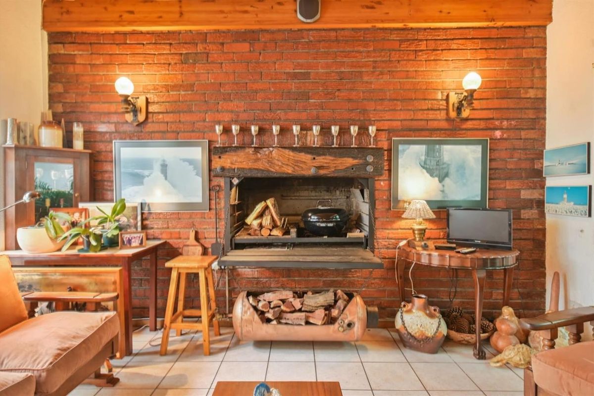 A living room featuring a prominent exposed brick wall with a built-in fireplace, timber mantelpiece, and ceramic floor tiles.