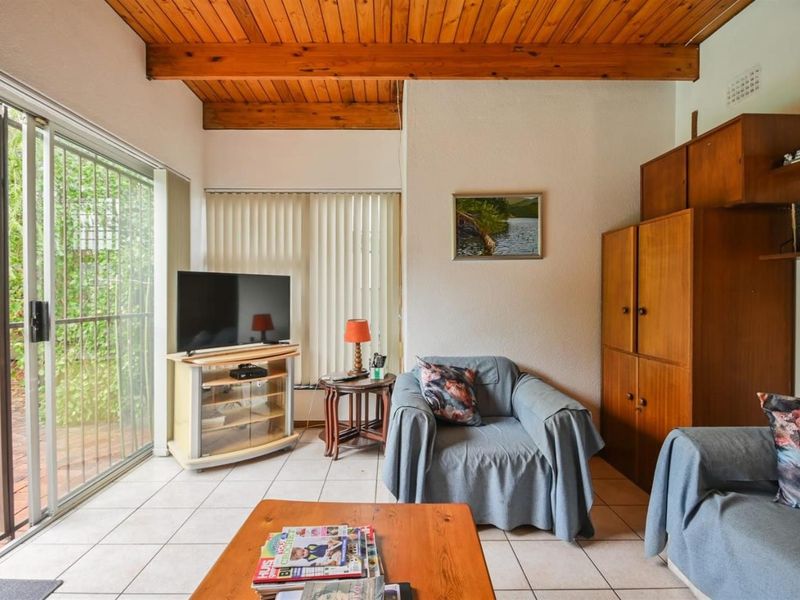 Living room featuring exposed timber ceiling beams, tiled flooring, and large sliding glass doors providing access to the outdoor area.