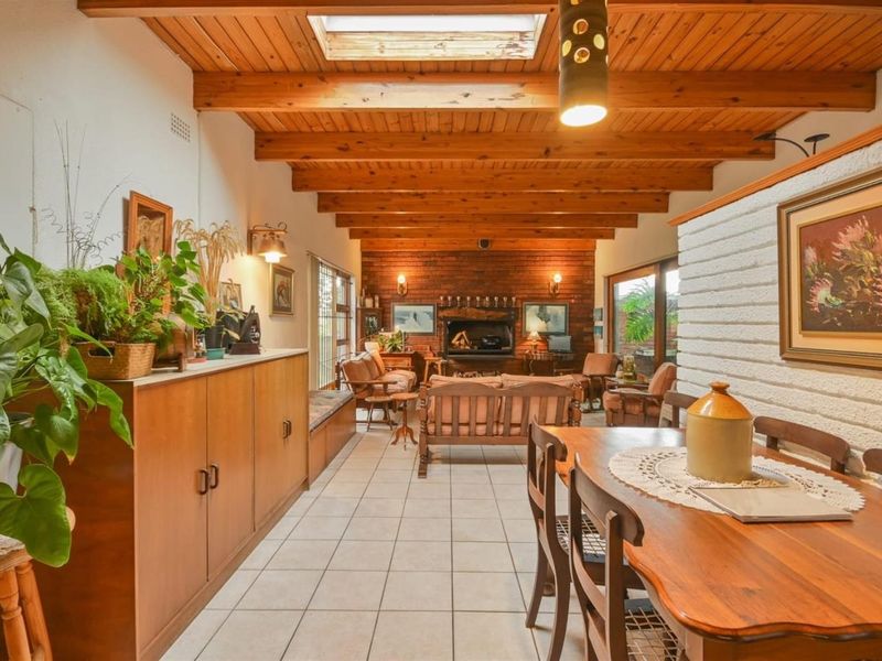 Spacious open-plan living and dining area featuring exposed timber beams, a skylight, and a prominent brick fireplace with tiled flooring throughout.