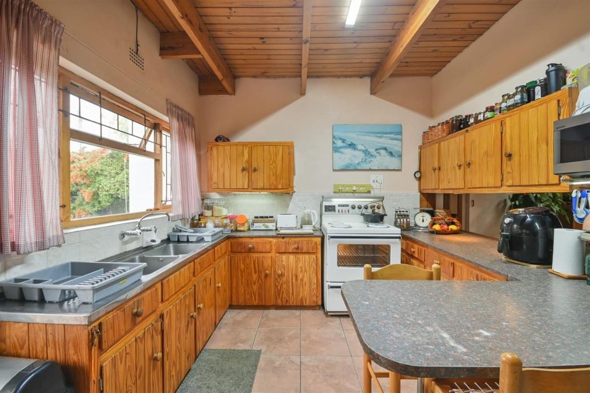 A functional kitchen featuring timber cabinetry, exposed ceiling beams, tiled flooring, and a double bowl stainless steel sink.