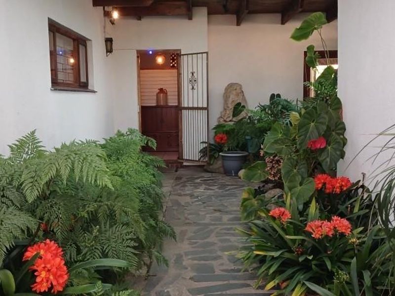 A charming covered patio area featuring exposed timber ceiling beams and natural stone paving, leading towards an entrance with a security gate.