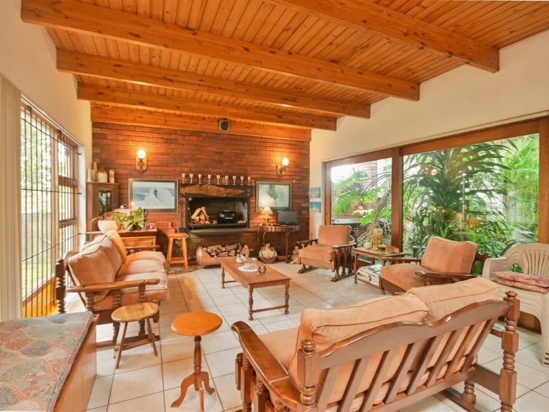 Spacious living room featuring a rustic brick fireplace, exposed timber beam ceiling, and large sliding glass doors that provide ample natural light.