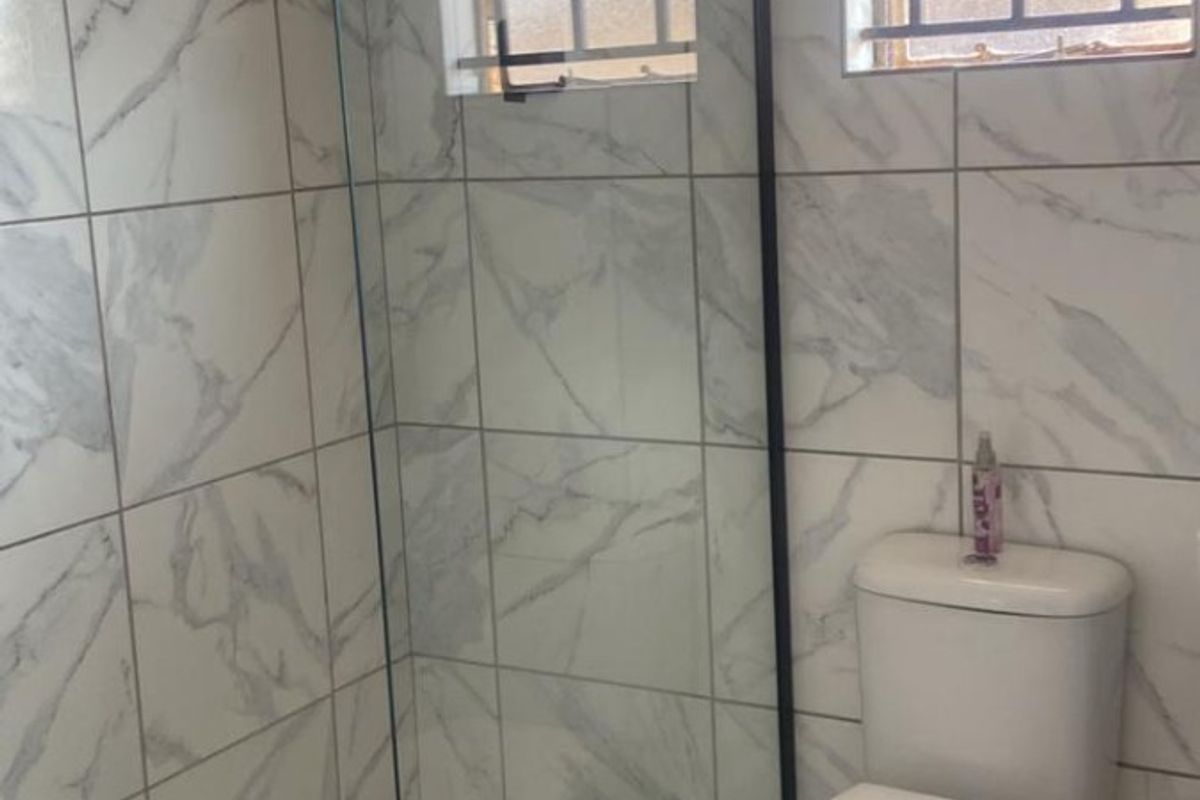 Modern bathroom featuring a walk-in shower with a rain shower head, marble-look wall tiles, hexagonal floor tiling, and a standard toilet.