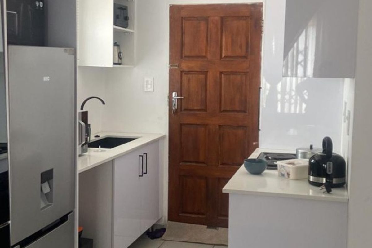 Compact kitchen featuring white cabinetry, tiled flooring, a built-in hob, and a solid wood door leading to the exterior.