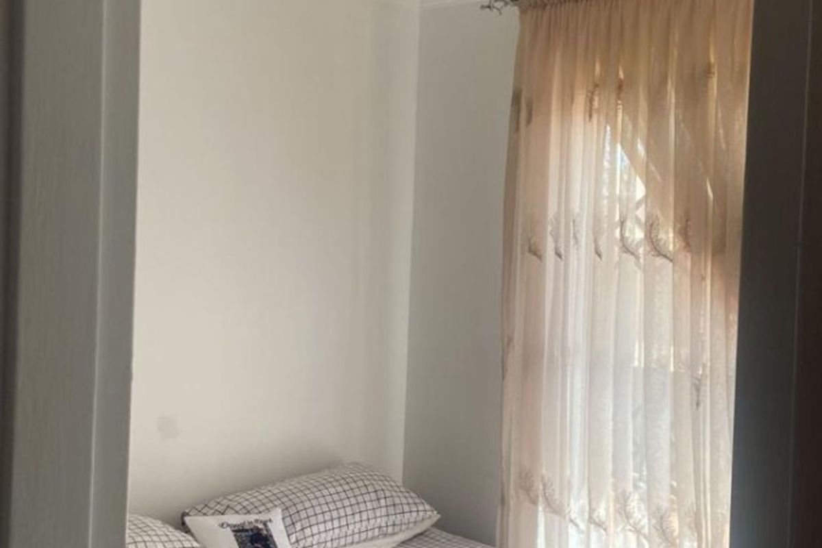 A compact bedroom featuring white walls, coving, and a window dressed with sheer curtains.