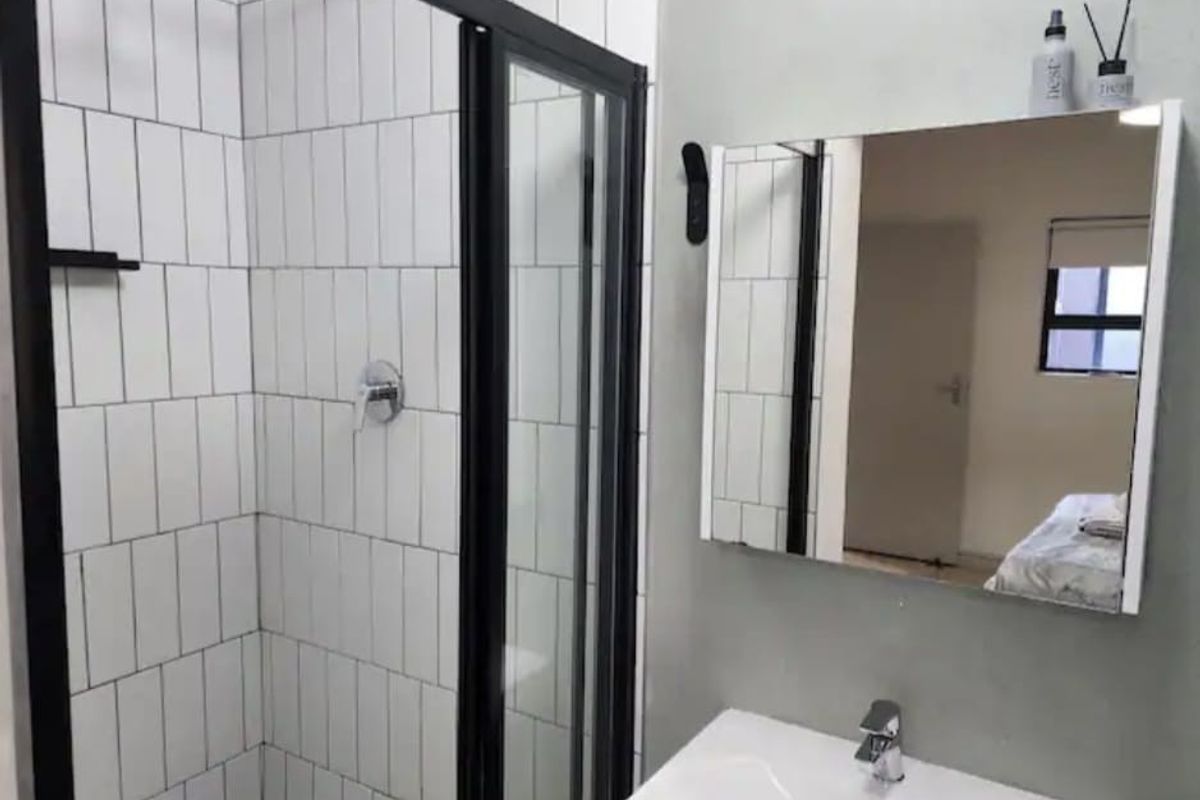 Modern bathroom featuring a walk-in shower with black frame, rain shower head, subway tiling, and a wall-mounted vanity mirror with basin.