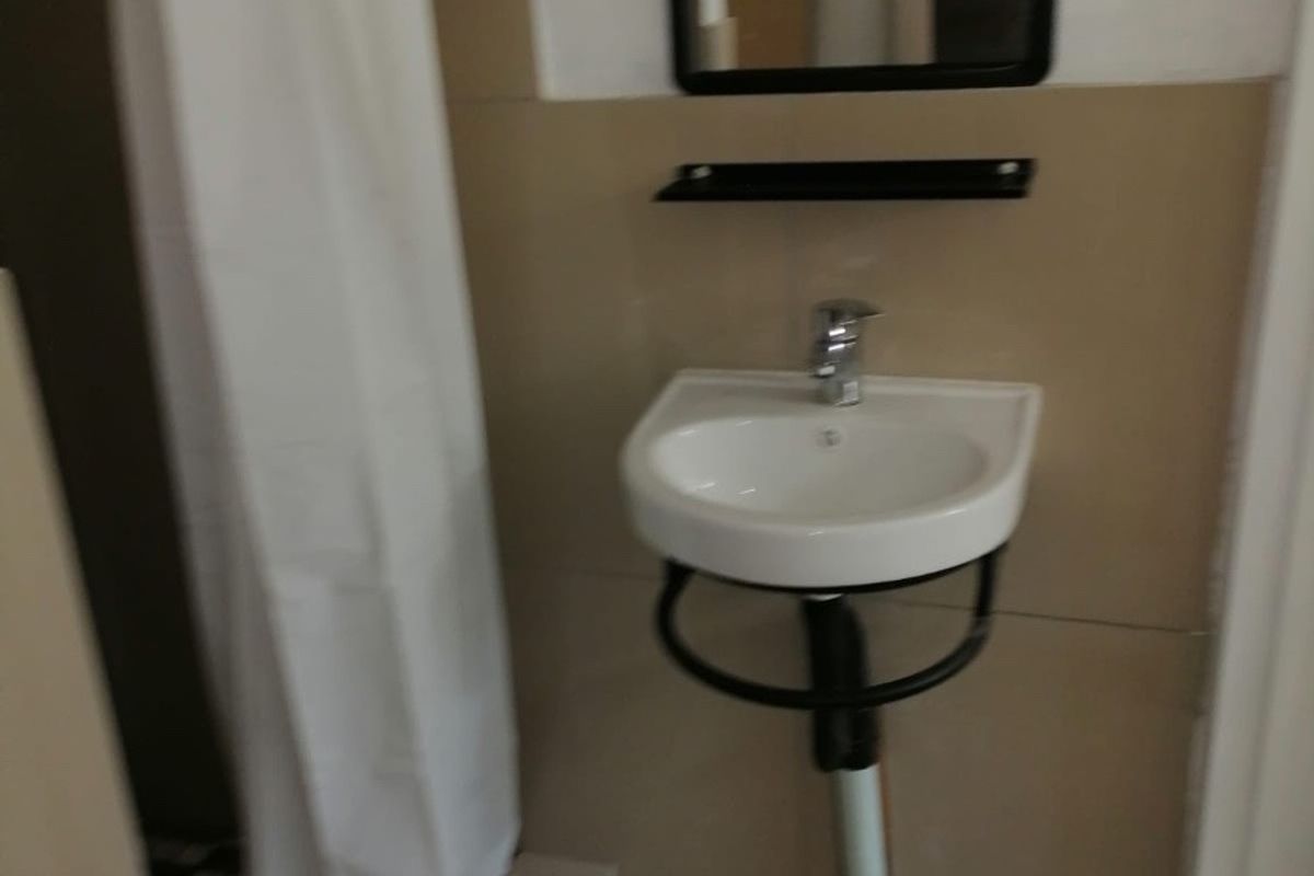 A small bathroom featuring a wall-mounted basin, tiled surfaces, and a shower area with a curtain.