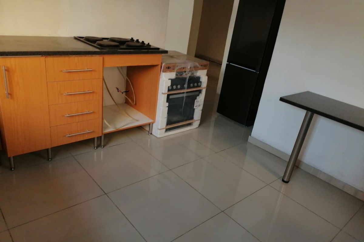 A kitchen area featuring built-in cabinetry, a hob, and tiled flooring, currently awaiting the installation of a built-in oven.