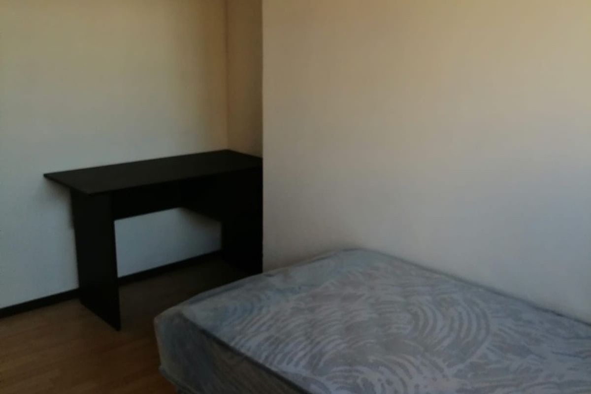 A simple bedroom featuring laminate flooring and neutral wall finishes, providing a functional space for rest or study.
