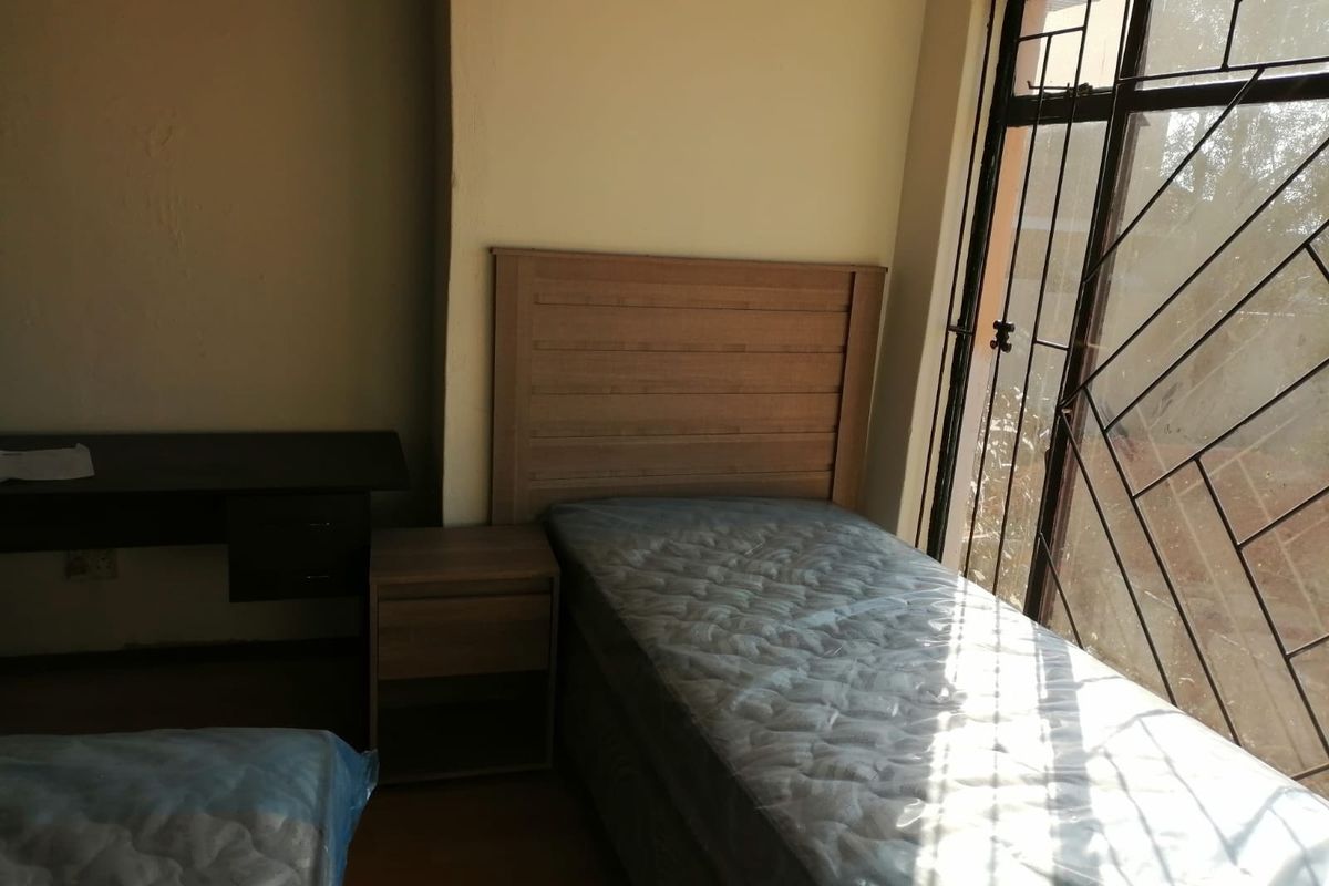 A bedroom featuring laminate flooring and a security gate on the window, requiring minor cosmetic updates to the wall finishes.