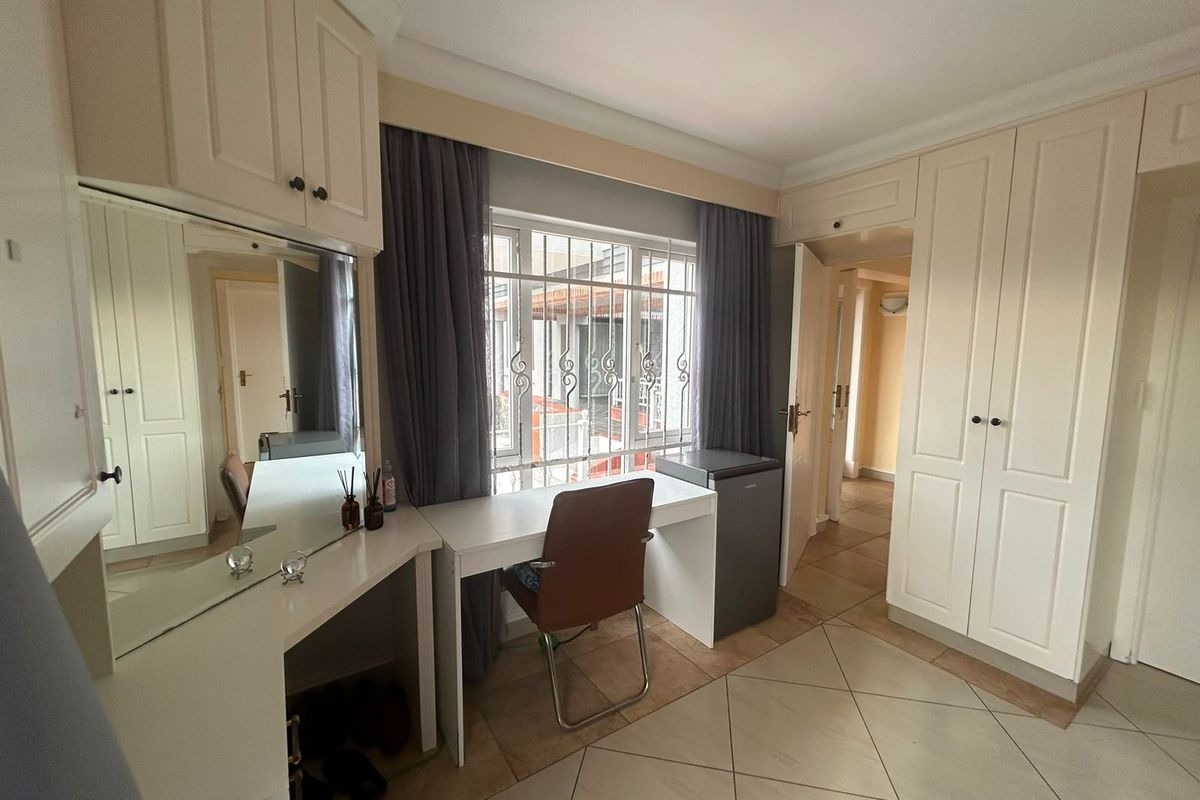 A bedroom featuring built-in cupboards, tiled flooring, and a vanity area with a mirror, complemented by security bars on the window.