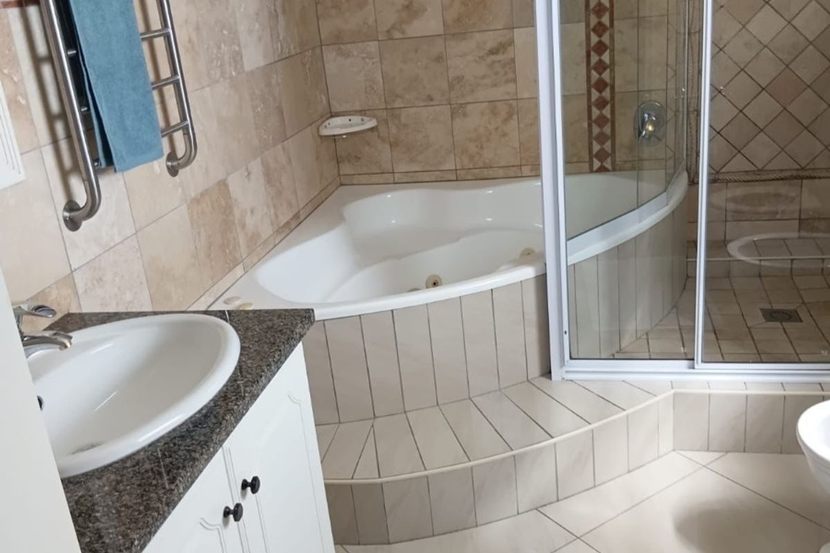 A well-appointed bathroom featuring a corner bathtub, a separate glass-enclosed shower, a vanity with granite countertop, and a heated towel rail.
