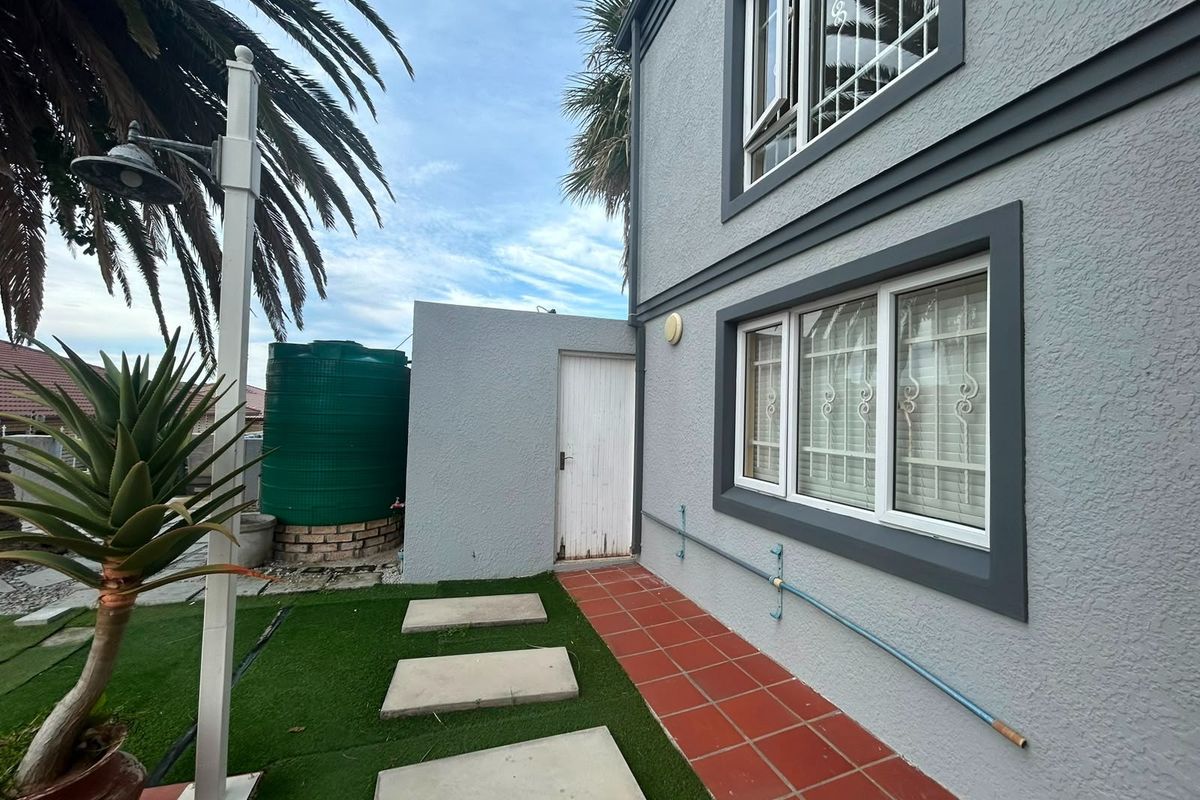 Rear exterior view of the lodge featuring a tiled pathway, artificial lawn, water storage tank, and security-fitted windows.