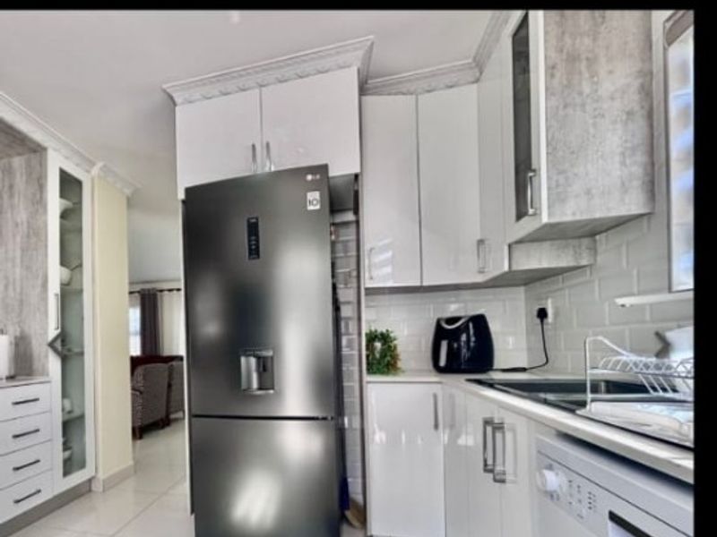 Modern kitchen featuring high-gloss white cabinetry, subway tile backsplash, and large format floor tiles, with integrated appliances and crown molding details.