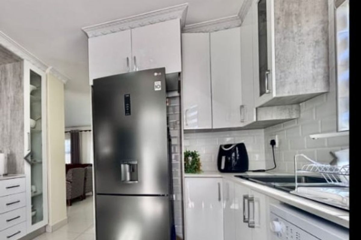 Modern kitchen featuring high-gloss white cabinetry, subway tile backsplash, and large format floor tiles, with integrated appliances and crown molding details.