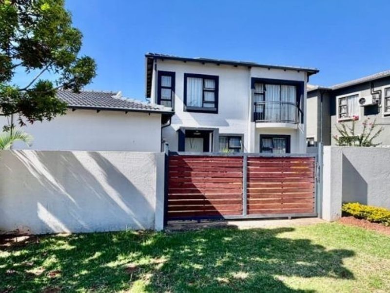 Front view of a two-story residential house featuring a perimeter wall, timber gate, and a balcony with aluminium window frames.