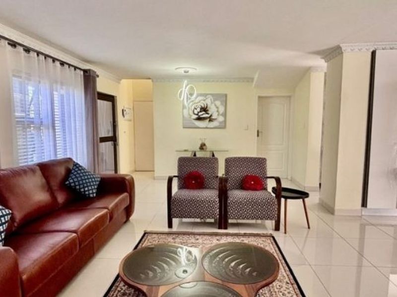 An open-plan living and kitchen area featuring tiled flooring, coved ceilings, and a modern kitchen with built-in appliances and a breakfast bar.