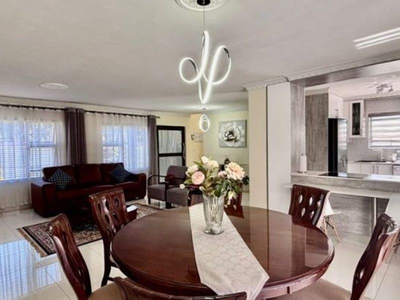 Spacious open-plan living and dining area featuring modern lighting, tiled floors, and a sleek breakfast bar connecting to a contemporary kitchen.