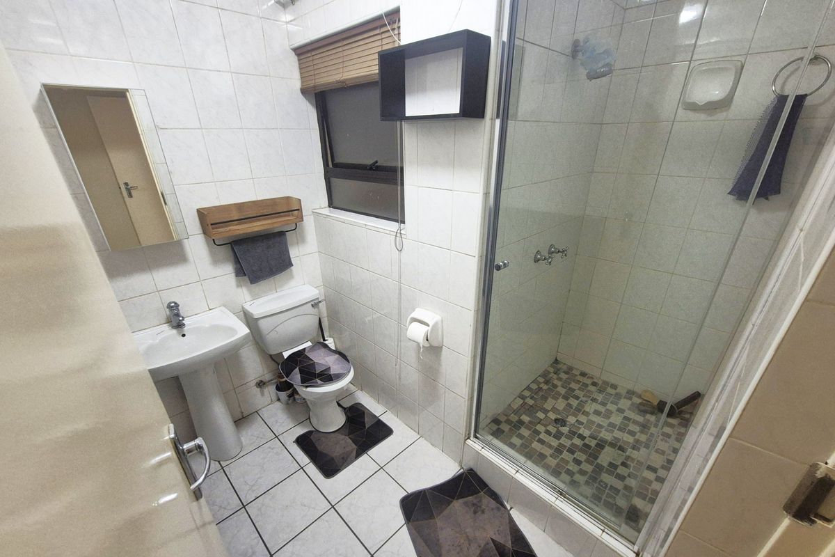 A functional bathroom featuring a pedestal basin, toilet, and a glass-enclosed shower with tiled finishes throughout.