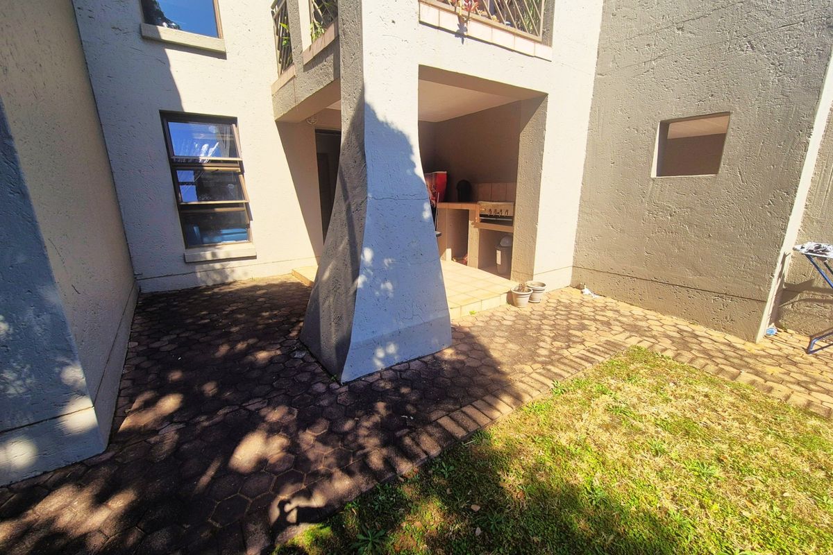Rear exterior view featuring a paved patio area with a built-in braai and access to an upper-level balcony.