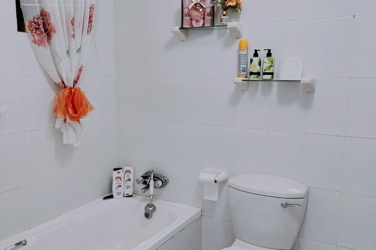 A functional bathroom featuring a standard bathtub, toilet, and white ceramic wall tiling with glass shelving for storage.