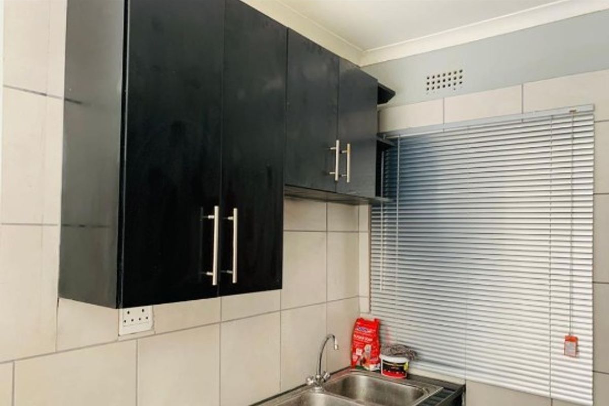 A functional kitchen area featuring black cabinetry, a double basin sink, tiled backsplash, and venetian blinds.