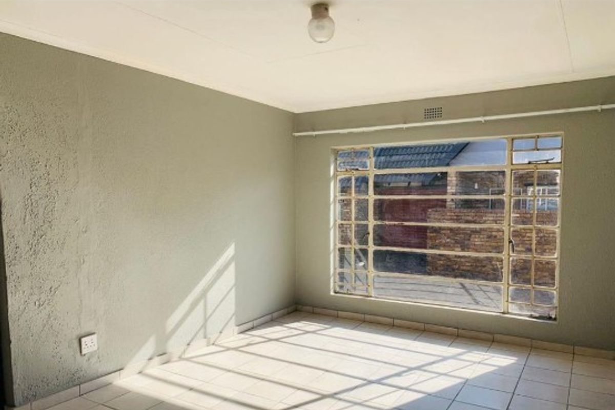 An empty living room featuring tiled flooring and a large steel-framed window, offering a blank canvas for potential interior design updates.