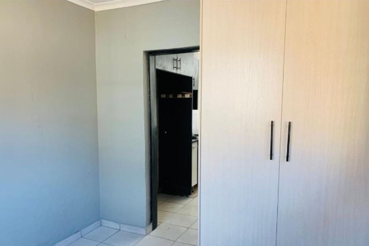 A bedroom featuring light-colored built-in wardrobes and tiled flooring, with a doorway leading to an adjacent room.