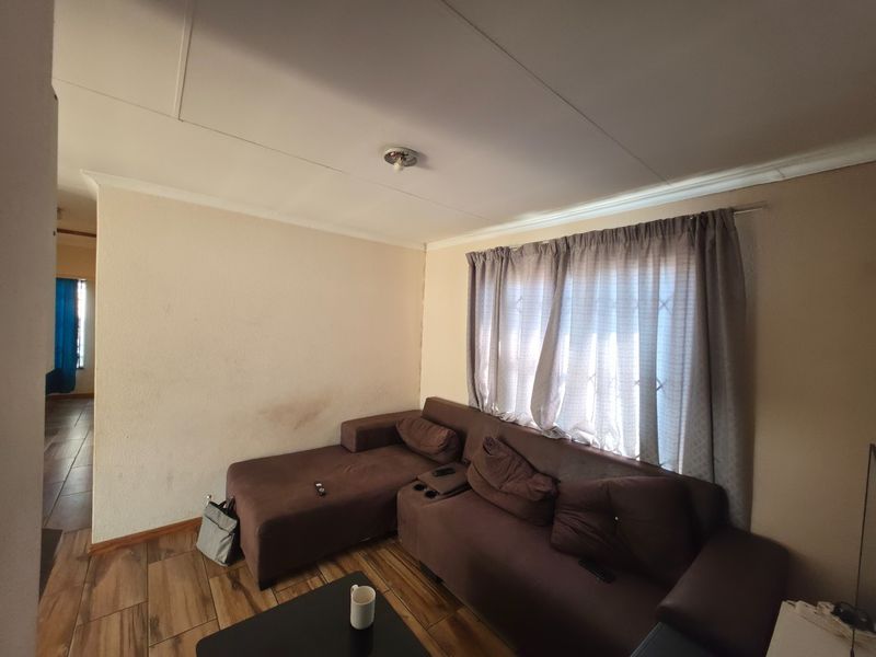 A living room featuring tiled flooring and a window with security bars, requiring minor cosmetic updates to the wall finishes.