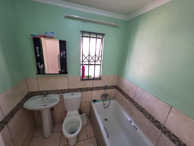 A functional bathroom featuring a pedestal basin, toilet, and bathtub with a handheld shower mixer, finished with tiled splashbacks and security window bars.
