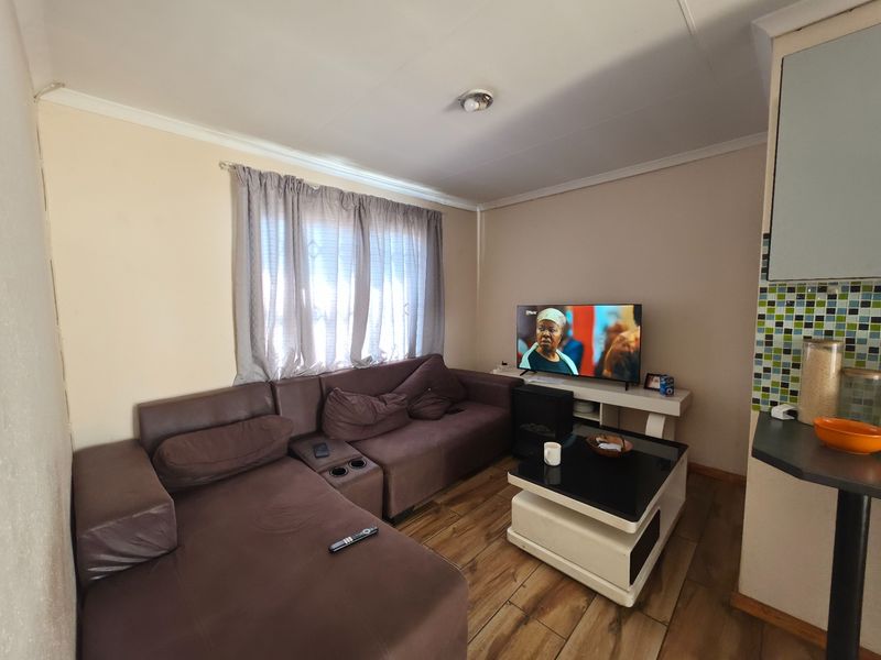Open plan living area featuring laminate flooring and a kitchen corner with mosaic tile backsplash.