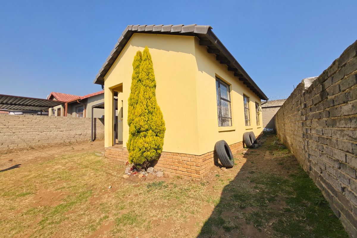 Rear view of the property showing the exterior facade, tiled roof, and perimeter walling with surrounding yard space.