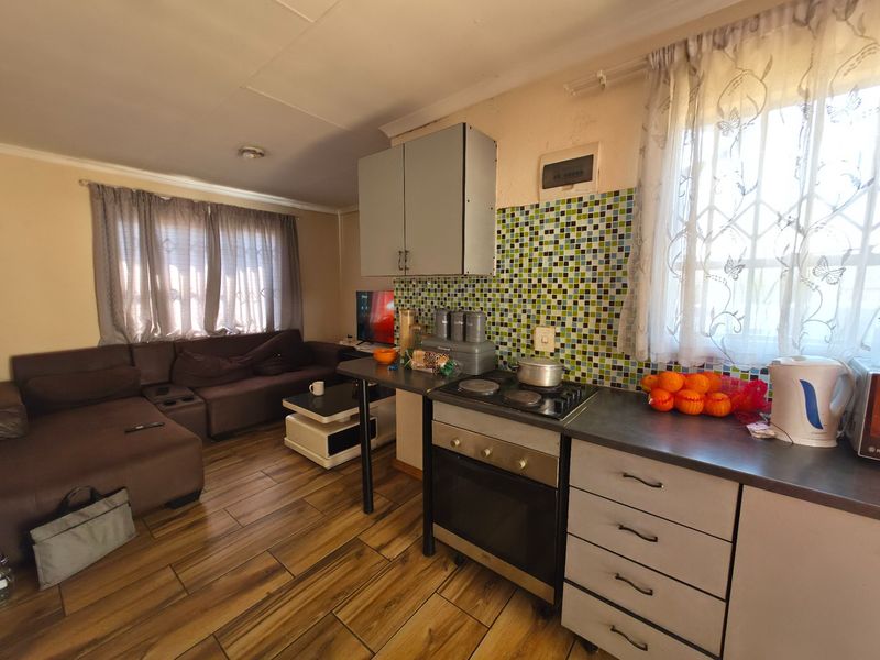 Open-plan living area featuring a compact kitchen with mosaic tile backsplash, built-in oven, hob, and laminate flooring throughout the combined space.