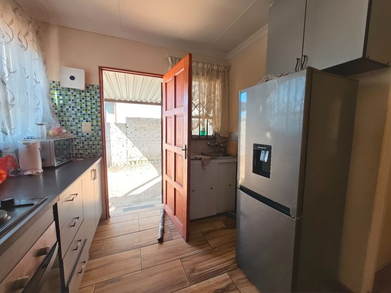 A functional kitchen featuring built-in cabinetry, tiled backsplash, and direct access to the exterior, offering a practical layout with potential for modern updates.