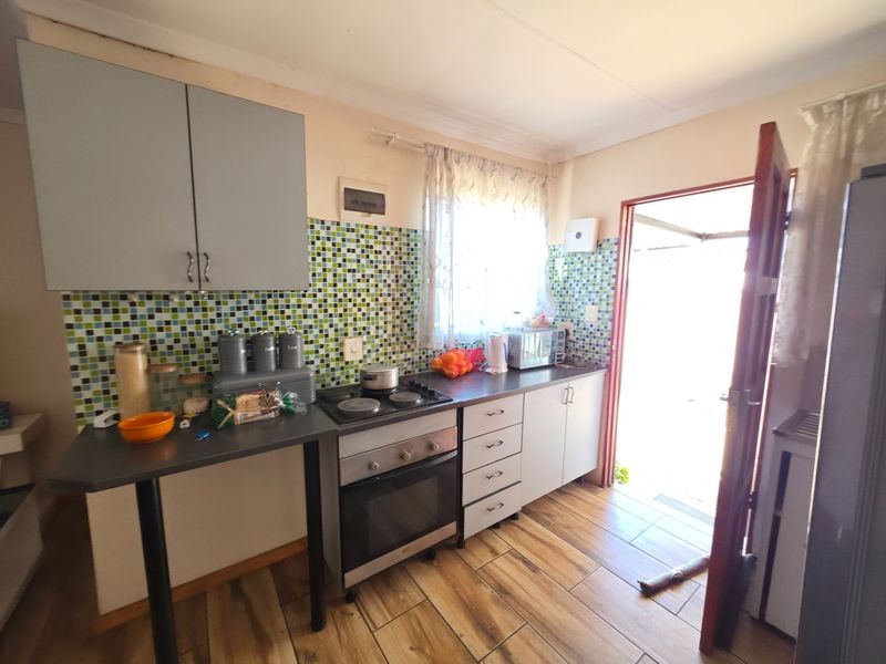 A functional kitchen featuring built-in cabinetry, an electric hob, oven, and a mosaic tile backsplash with direct access to the exterior.