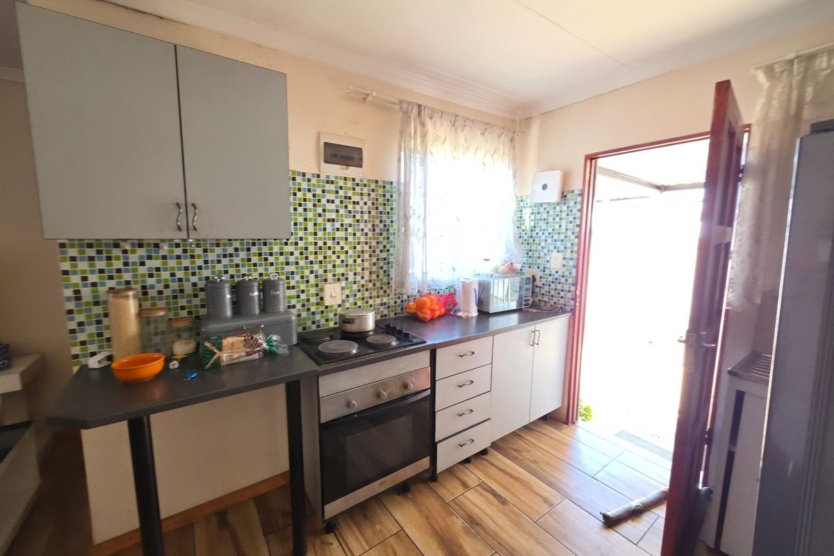 A functional kitchen featuring built-in cabinetry, an electric hob, oven, and a mosaic tile backsplash with direct access to the exterior.