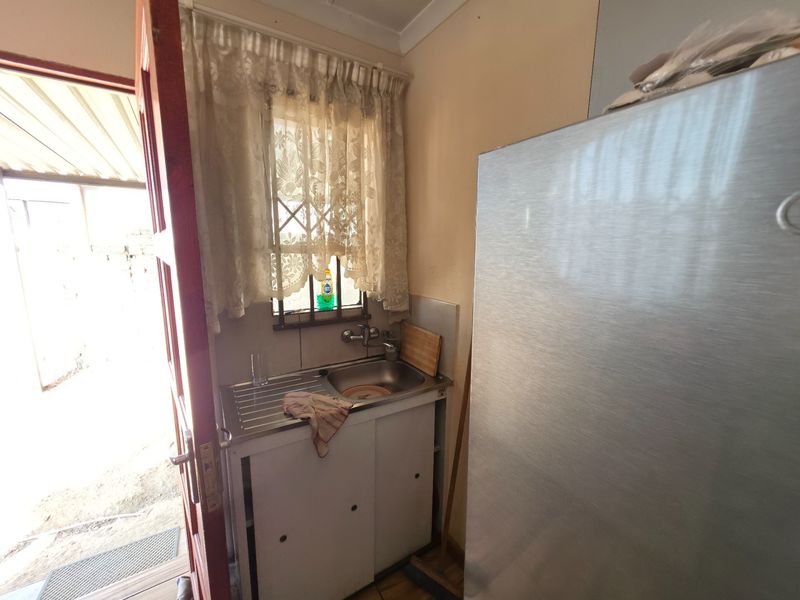 A compact scullery area featuring a stainless steel sink, tiled splashback, and direct access to the exterior through a side door.
